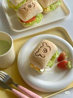 two plates with sandwiches and strawberries on them, one has a face drawn on it