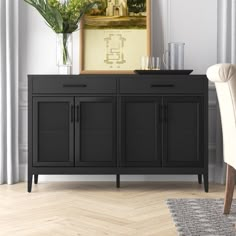 a black cabinet sitting next to a chair in a living room with a painting on the wall