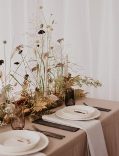 the table is set with white plates and flowers