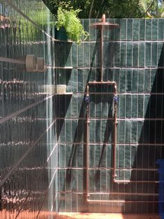 an outdoor shower with green tiles and metal bars on the wall, next to a blue trash can