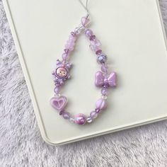 a purple beaded necklace with pink hearts and a teddy bear on it, sitting on a white surface