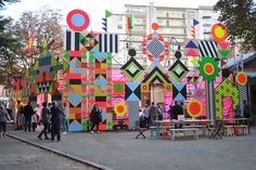 people are standing in front of an art installation on the side of a building that is decorated with colorful geometric shapes