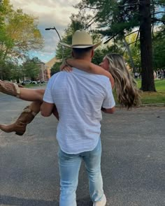 a man carrying a woman on his back while walking down the street in front of some trees