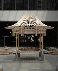 a wooden gazebo sitting on top of a cement floor next to a tall building