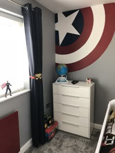 a room with a captain america mural on the wall and a white chest of drawers