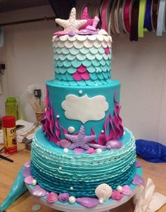 a three tiered cake decorated with blue, pink and white under the sea theme