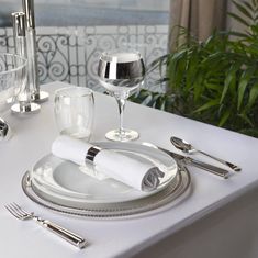 a white table with silverware and wine glasses on it, along with place settings