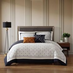 a bed with white and black comforter in a bedroom next to a lamp on a wooden floor