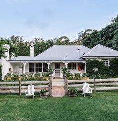 a white house with two lawn chairs in front of it and green grass around the yard