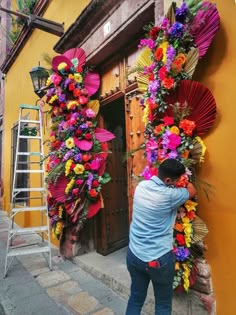 a man standing next to a yellow building with flowers on the outside and behind him