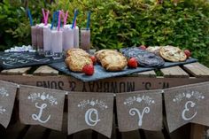 a table topped with cookies and desserts on top of a wooden table next to bushes