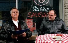 two men sitting at a table in front of a restaurant