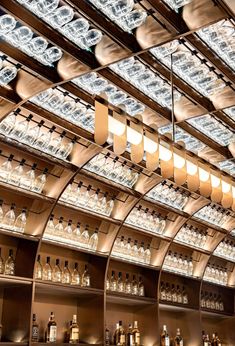 a bar with many bottles and lights on the ceiling in front of glass shelves filled with liquor