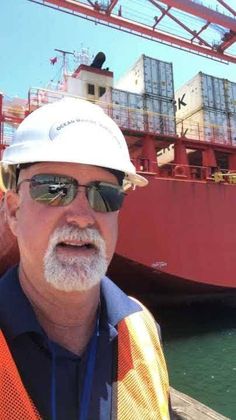 a man in safety vest and hard hat standing next to a large ship with cargo containers on it