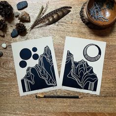 two cards with black and white designs on them next to a pen, feather, and some other items