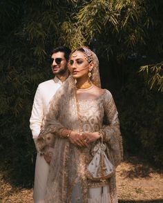 a man and woman standing next to each other in front of some trees wearing wedding outfits