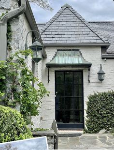 a white brick house with a black door and glass window in the front yard, surrounded by greenery