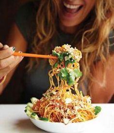 a woman eating noodles with chopsticks in her hand and smiling at the camera