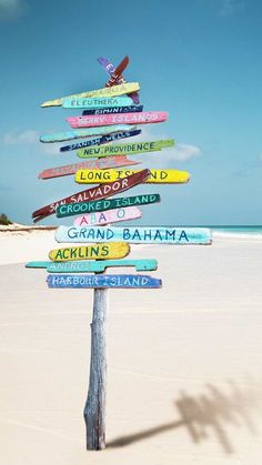 a wooden pole with many different colored signs attached to it's sides on the beach