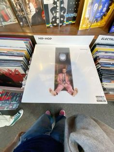 a person sitting on the floor in front of a book shelf filled with books and cds