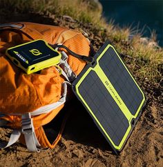 an orange backpack with a solar panel attached to it sitting on the ground next to some water