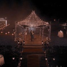 a man and woman standing under a lit up gazebo in the middle of a field