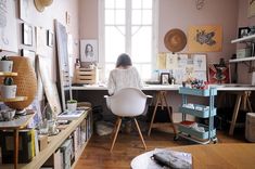 a woman sitting at a desk in an art studio with lots of artwork on the walls