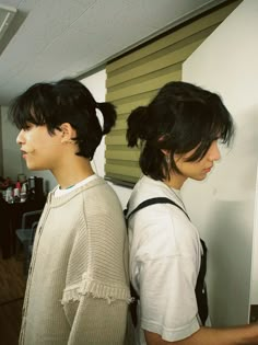 two young people standing next to each other in front of a wall with blinds on it