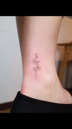 a small flower tattoo on the side of a woman's ankle, with pink flowers