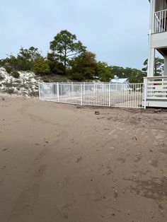 a white fence is in front of a house on the beach with sand around it