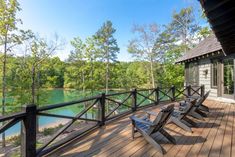 a deck with two chairs and a view of a lake in the woods behind it