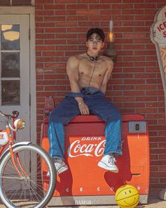 a man sitting on top of a coca - cola cooler next to a yellow ball