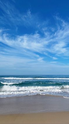 two people walking on the beach with surfboards under a partly cloudy blue sky,