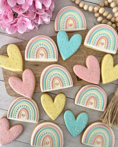 decorated cookies with pastel rainbows and hearts on a wooden board next to pink flowers