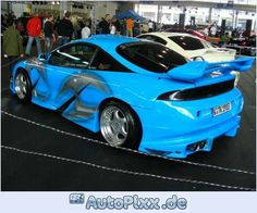 two blue sports cars parked next to each other in a showroom with people looking at them