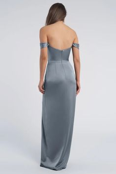 the back of a woman wearing an off shoulder grey gown with one side slit open