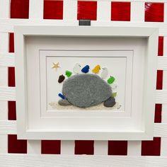 a rock in the sand with sea shells and starfish on it under a white frame