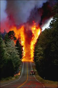 a large fire is burning on the side of a road with cars driving down it