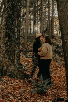 two people standing next to each other in the woods with leaves on the ground and trees