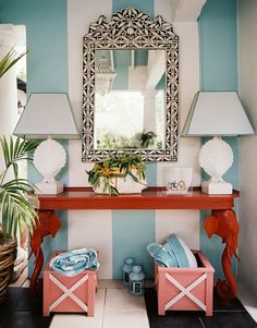 a room with blue and white stripes on the walls, a red console table and two pink stools