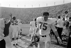 an old black and white photo of football players walking off the field with their hands in the air