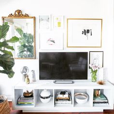 a white entertainment center with lots of pictures on the wall and plants in vases