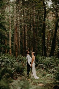 a bride and groom standing in the woods