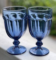 two blue glass goblets sitting on top of a window sill next to each other