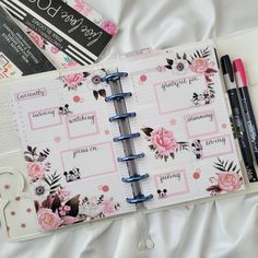 an open planner book with pink flowers on it and two pens laying next to it