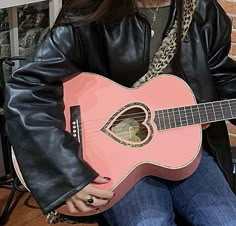 a woman holding a pink guitar in front of her face and wearing a black jacket