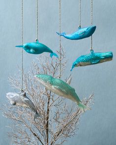 three ornaments hanging from chains in the shape of dolphins and seaweed on a tree branch