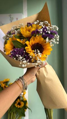 a woman holding a bouquet of sunflowers and other flowers in her hand,