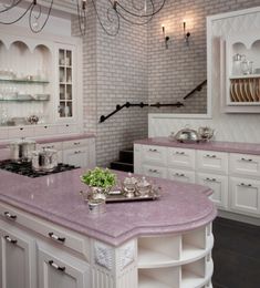 a kitchen with white cabinets and pink counter tops, an island in the middle is surrounded by hanging chandeliers