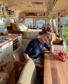 a woman sitting at a kitchen table in a camper with lots of furniture and decor